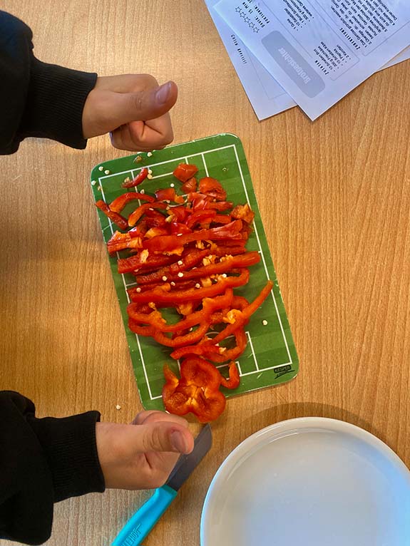 Ein Brett mit geschnittener Paprika und Kinderhänden die die Daumen nach oben zeigen